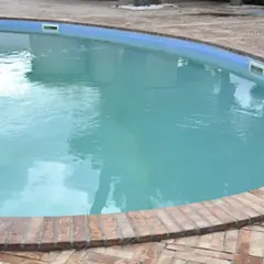 Agua de piscina blanquecina, con reflejos del cielo y rodeada por un borde de ladrillos.