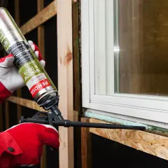 Persona con guantes rojos aplica espuma de poliuretano alrededor de una ventana. Averigua cuanto tarda en secar la espuma de poliuretano para un sellado perfecto.