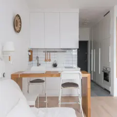 Interiores de casas sencillas con cocina blanca, barra de madera y sofá blanco. Estilo minimalista y funcional.
