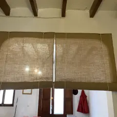 Dos estores enrollables caseros de tela de yute cubren una ventana. La luz del sol se filtra a través de ellos.