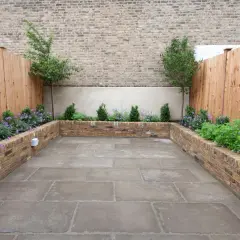 Un patio moderno con jardineras de ladrillo para decorar poyete ventana exterior. Plantas verdes y flores moradas crean un oasis urbano.