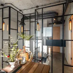 Interior moderno con paredes de cristal, lámparas colgantes y un arreglo floral sobre una mesa de madera.