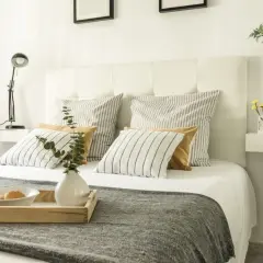 Cama con cabecero blanco, cojines a rayas y mostaza, y bandeja con desayuno. Ideas para como tapizar un cabecero.