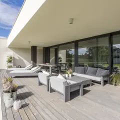 Terraza moderna con muebles grises y una puerta corredera elevable o osciloparalela que da a un jardín verde.