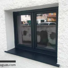 Ventana con marco oscuro y un alféizar negro que funciona como vierteaguas, protegiendo la pared de la lluvia.