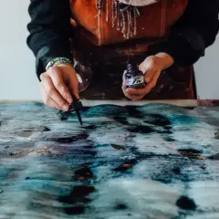Manos aplicando tinta a un lienzo texturizado, como enmarcar un lienzo con arte abstracto.