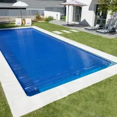 Piscina cubierta con persiana azul, lista para climatizar y disfrutar. Césped verde y tumbonas invitan al relax.
