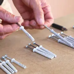 Man manipula un taco químico para pared, preparándolo para fijar algo.