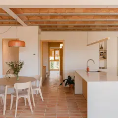Interior de una vivienda antigua renovada, con suelo de terracota, vigas de madera a la vista y cocina moderna.