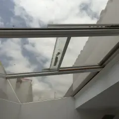 Techos de cristal inconvenientes: suciedad y óxido en los marcos, reflejando un cielo nublado y edificios.