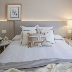 Elegantes ideas de habitaciones de matrimonio con cama blanca, cojines decorativos y mesita de noche con lámpara.