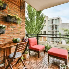 Un balcón alargado decorado con muebles de madera, cojines rojos y plantas colgantes. Un espacio acogedor para disfrutar del exterior.