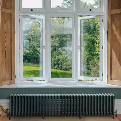 Ventanas blancas abiertas a un jardín verde, con cortinas florales y un radiador antiguo. Las mejores ventanas para disfrutar del exterior.