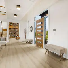 Amplio vestíbulo con suelo de vinilo autoportante de madera clara, puerta principal de madera, escaleras y estanterías.