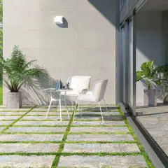Terrazas pequeñas con encanto, con baldosas y césped, mesa y sillas blancas, plantas y vista a un jardín verde.