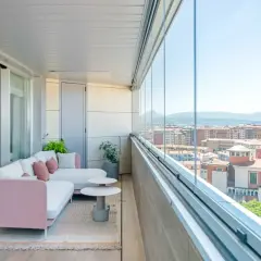 Sofá rosa y blanco en terrazas acristaladas con decoración moderna. Disfruta de la vista urbana desde este espacio acogedor.