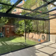 Modernos tejados para porches de cristal, con vistas a un jardín con caseta de madera y árboles frondosos.
