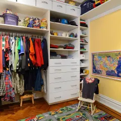 Armario infantil con ropa colgada en la barra, estantes con juguetes y cajones. La altura de la barra del armario es perfecta para los niños.