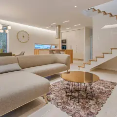 Elegantes ideas de interiores de casas: sofá moderno, mesa de centro dorada, alfombra circular y escaleras de madera flotantes.