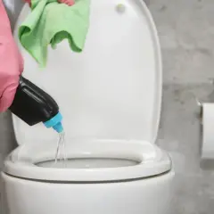 Mano con guante rosa vierte agua fuerte para que sirve en el inodoro. Paño verde en mano.