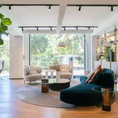 Amplio salón con sofás curvos, sillones, mesas de centro y estanterías, todo bañado por luz natural a través de grandes ventanas modernas.