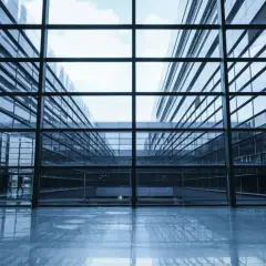 Interior de un edificio moderno con amplios muros cortina de cristal que reflejan el cielo y la arquitectura circundante.