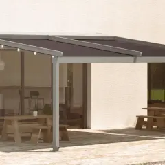 Pérgola moderna con techo oscuro, ideal para saber como cubrir un patio de la lluvia y disfrutar del exterior. Mesas de madera y zona ajardinada.
