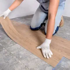 Manos enguantadas colocando una tabla de suelo vinílico sobre un suelo de hormigón.