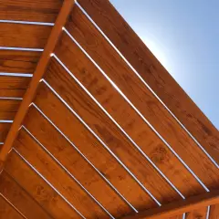 Vistas desde abajo de una estructura de madera con tratamiento para exterior, con el cielo azul brillante entre las lamas.