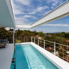 Una moderna piscina en ático con vistas a un paisaje verde. Un sofá gris y una mesa de centro completan el espacio.