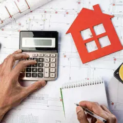 Manos calculando presupuesto para obras de reforma. Planos, calculadora, cinta métrica y casa roja.