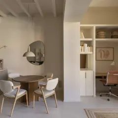 Comedor y zona de trabajo en mini pisos. Mesa redonda, sillas blancas, escritorio con silla de cuero y estanterías.