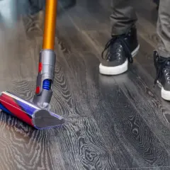 Persona aspira el suelo de vinilo con una aspiradora de mano. El suelo tiene un patrón de madera oscura.