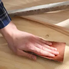 Mano lijando madera con lija, preparando la superficie para un acabado perfecto.