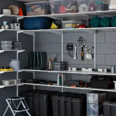 Estanterías metálicas con todo tipo de objetos: cajas, herramientas, botas de agua, botellas. Un ejemplo de cómo organizar un trastero.