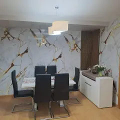 Comedor moderno con pared de mármol y oro, sillas negras y aparador blanco. El cloruro de polivinilo (PVC) es un material versátil.