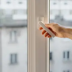 Mano girando la manija de una ventana osciloparalela, quizás para solucionar problemas de apertura o cierre.