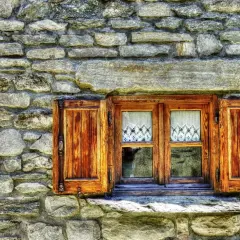 Ventana de madera con contraventanas abiertas, lista para restaurar. Cortinas de encaje blanco adornan los cristales.