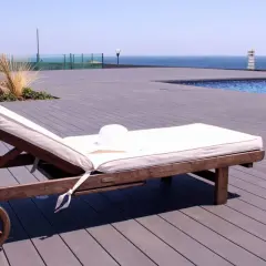 Tumbona lista para el sol sobre una terraza de madera composite, con piscina y mar al fondo.