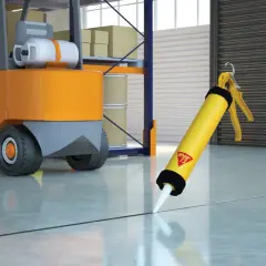 Pistola de Sikaflex lista para sellar juntas en un almacén, con una carretilla elevadora al fondo. Sikaflex para que sirve: sellar y unir.