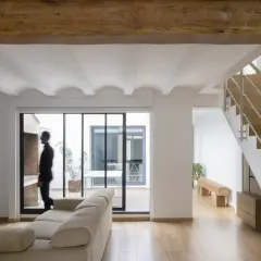 Interior moderno con vigas de madera, escaleras y un hombre mirando al patio. Estimación del precio construir casa 30 m2.