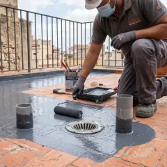 Obrero aplica pintura gris para impermeabilizar terraza. Rodillo y cubeta de producto a su lado.