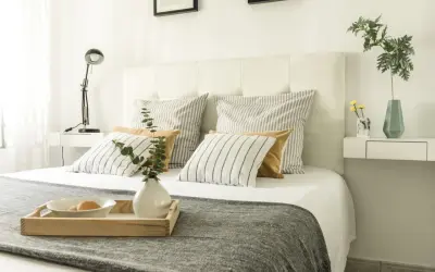 Cama con cabecero blanco, cojines a rayas y mostaza, y bandeja con desayuno. Ideas para como tapizar un cabecero.