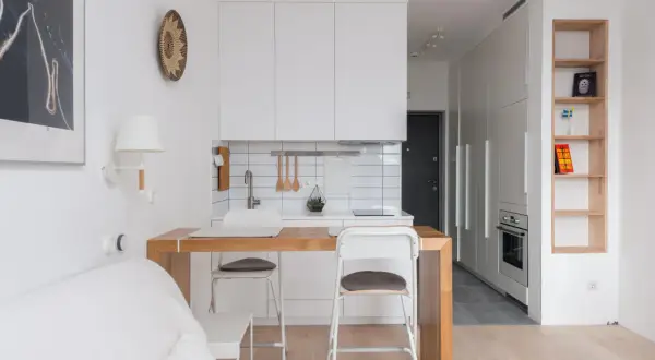 Interiores de casas sencillas con cocina blanca, barra de madera y sofá blanco. Estilo minimalista y funcional.