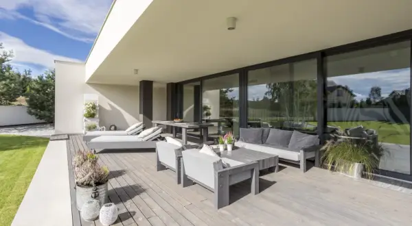 Terraza moderna con muebles grises y una puerta corredera elevable o osciloparalela que da a un jardín verde.