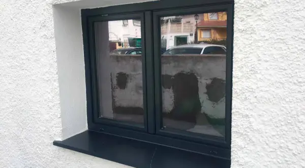 Ventana con marco oscuro y un alféizar negro que funciona como vierteaguas, protegiendo la pared de la lluvia.