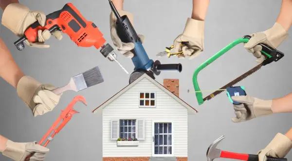 Manos con guantes sostienen herramientas de construcción alrededor de una casa. ¡Calcula tu reforma casa precio!