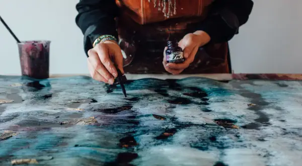 Manos aplicando tinta a un lienzo texturizado, como enmarcar un lienzo con arte abstracto.