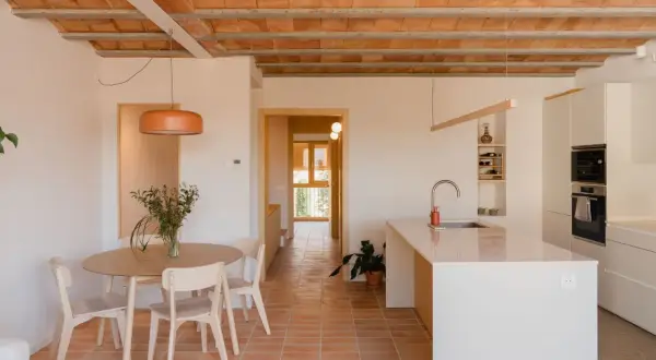 Interior de una vivienda antigua renovada, con suelo de terracota, vigas de madera a la vista y cocina moderna.
