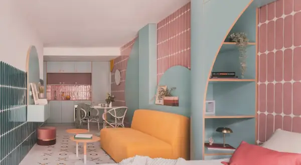 Habitación de 4 metros cuadrados con sofá amarillo, estanterías turquesas y detalles en rosa. Cocina y comedor integrados.